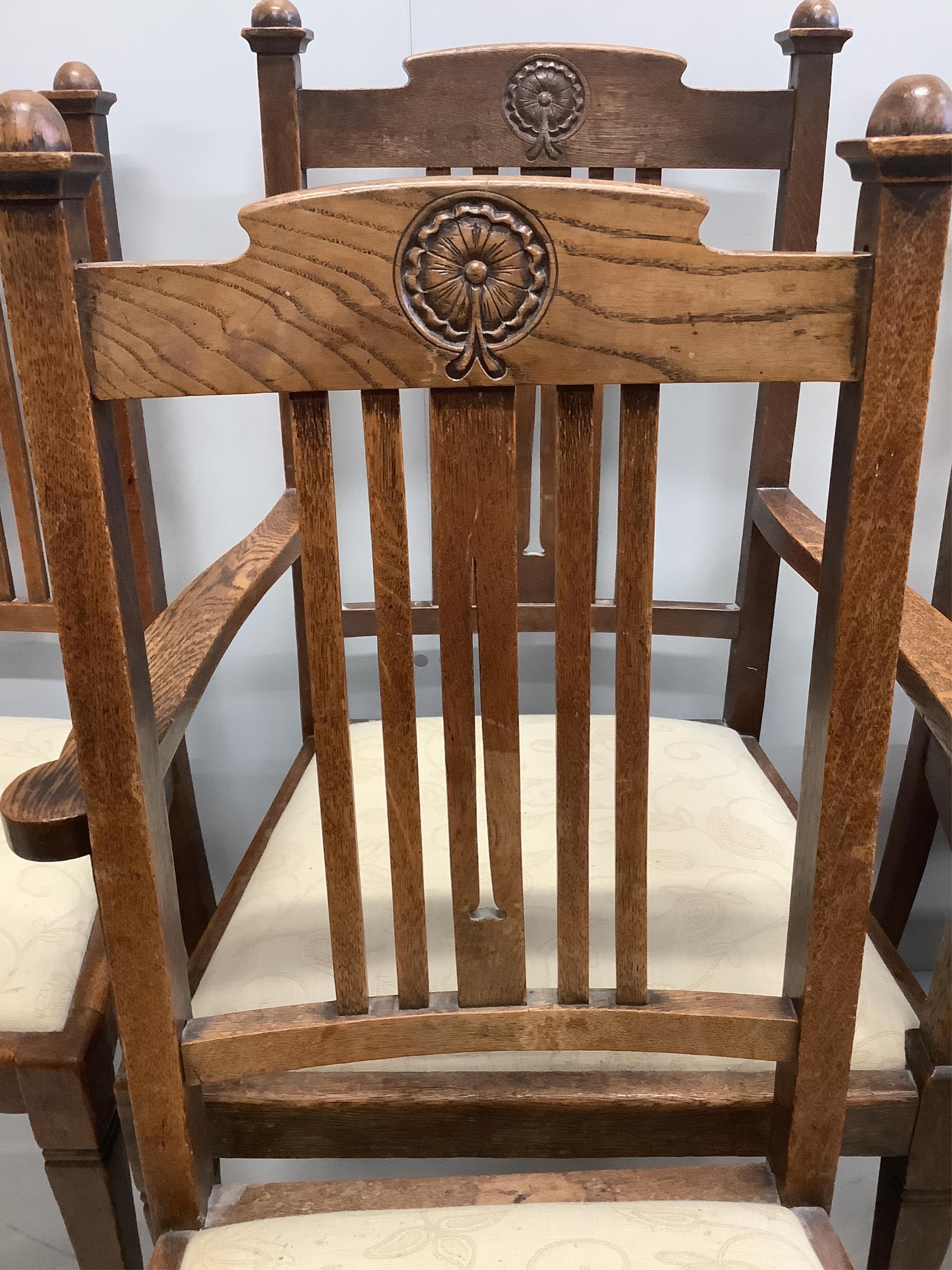 A set of six Arts & Crafts oak rail back dining chairs, with rosette carved crest rails, two with arms. Condition - fair